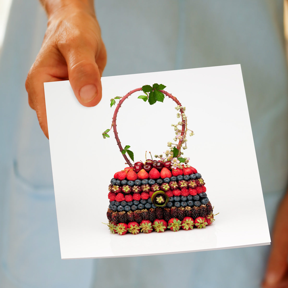 A model holds a fresh berry bag greeting card from Golly Gosh Creations. Handcrafted from fresh berries it's sitting on a white background.
