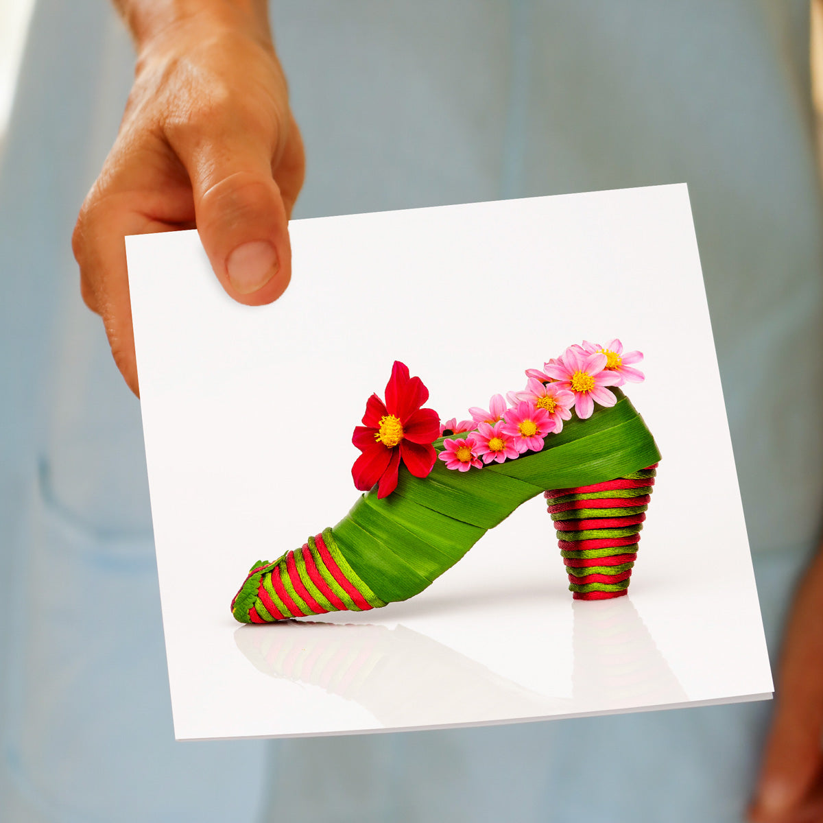 A hand held dahlia shoe greeting card. This quality square card is from Golly Gosh Creations. Crafted from vibrant dahlia blooms and flax foliage.