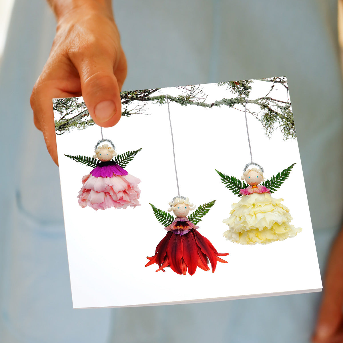 Hand holding the Christmas Angel Trio greeting card, showing the flower angel design