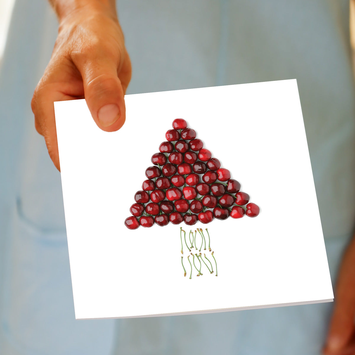 Hand holding the Christmas Cherry Tree greeting card, showing the cherry tree design