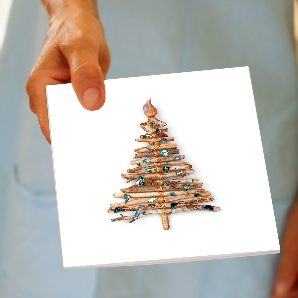 Hand holding the Christmas Driftwood Tree greeting card, showing the driftwood and paua shell design