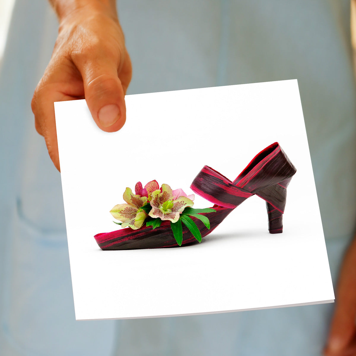 A helleborus flax shoe greeting card being hand held. This quality square card is available at Golly Gosh Creations.