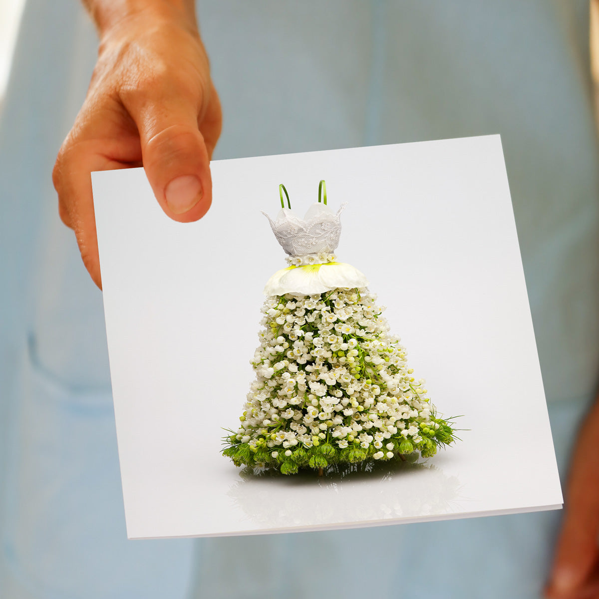 Hand holding Lace Bodice Dress greeting card featuring elegant floral gown made of white flowers with green accents