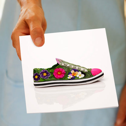 A pansy shoe greeting card being held by hand. Found at Golly Gosh Creations, this generous square card is created with colourful dainty pansies.