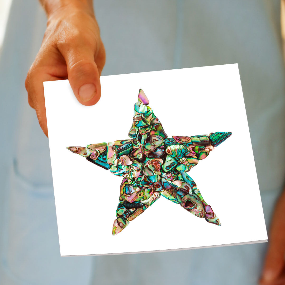 A paua star greeting card from Golly Gosh Creations being held by hand. This shimmering card is created from pieces of  iridescent paua shell.