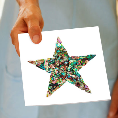 A paua star greeting card from Golly Gosh Creations being held by hand. This shimmering card is created from pieces of  iridescent paua shell.