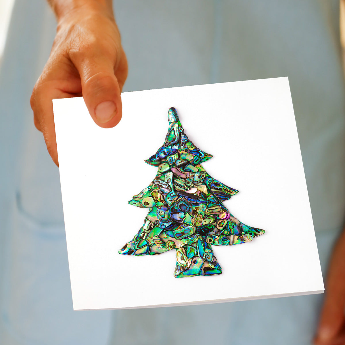 Hand holding the Christmas Paua Tree greeting card, showing the paua shell design