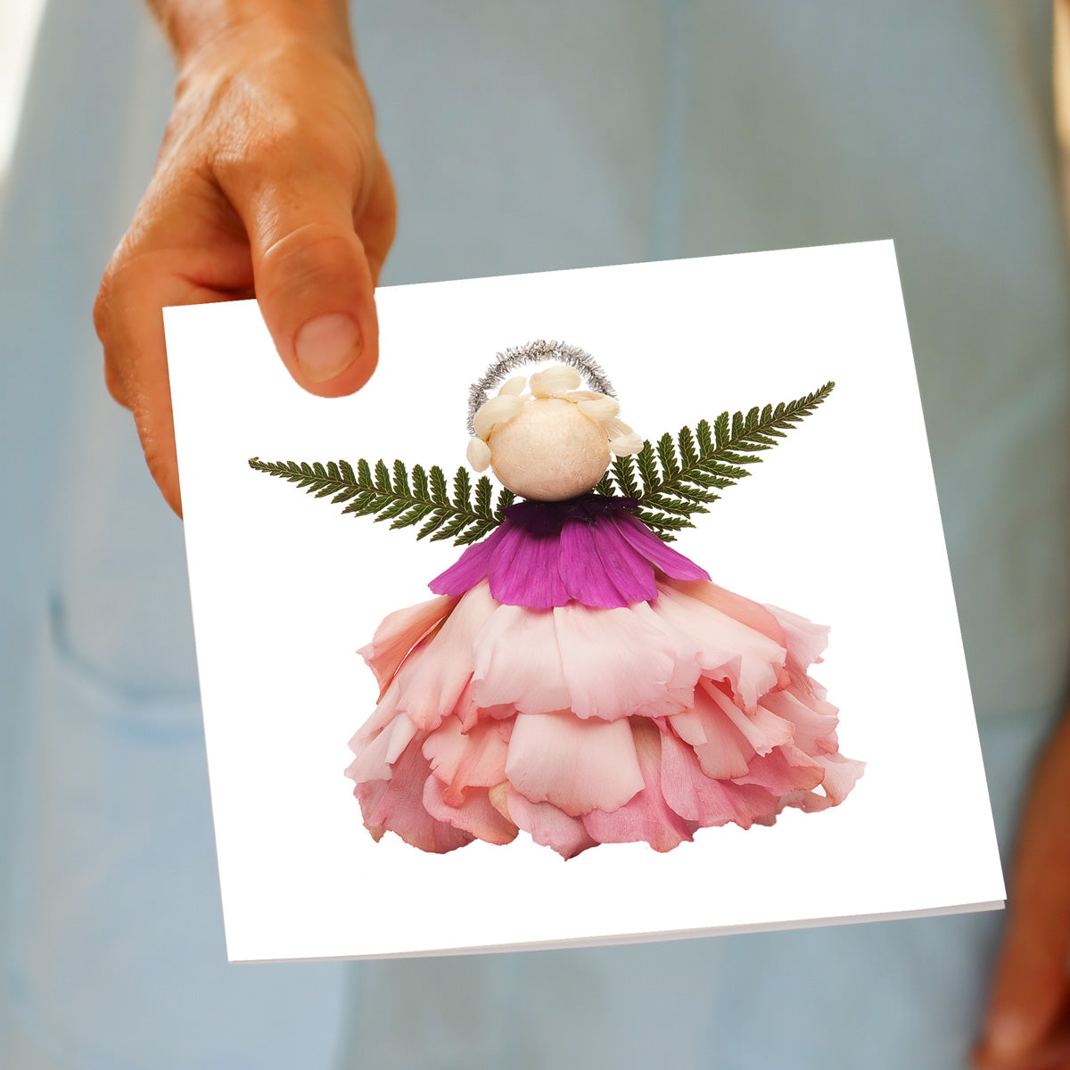 Hand holding the Christmas Pink Angel greeting card, showing the pink flower angel design