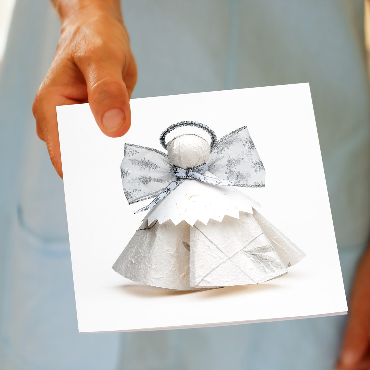 Hand holding the Christmas Silver Angel greeting card, showing the paper angel design
