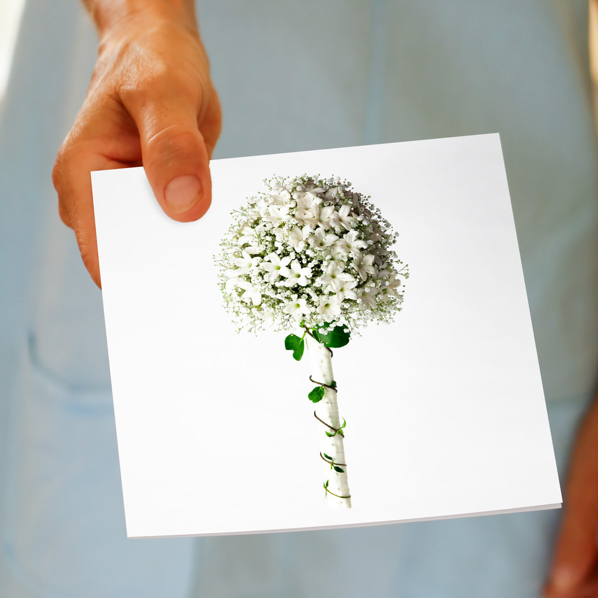 A stephanotis and gypsophila bouquet greeting card. being held by hand. A stunning arrangement on a white background. Size 142 x 142 mm